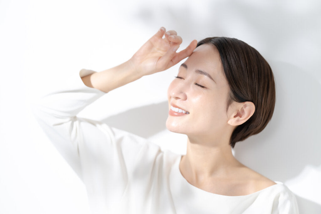 Smiling woman shielding her eyes from sunlight, highlighting how UPF clothing and sunscreen work together to block, reflect, and absorb harmful UV rays.