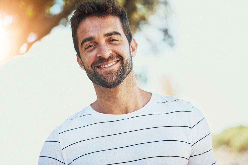 Man smiling outdoors in a lightweight UPF shirt, illustrating how sun-protective clothing helps prevent skin cancer through daily UV protection.