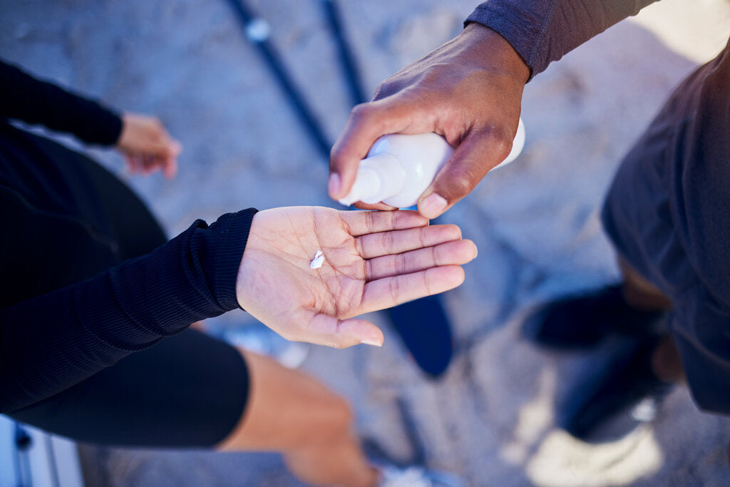 Close-up of two people at the beach applying sunscreen, emphasizing the importance of sun protection for all skin tones during outdoor activities.