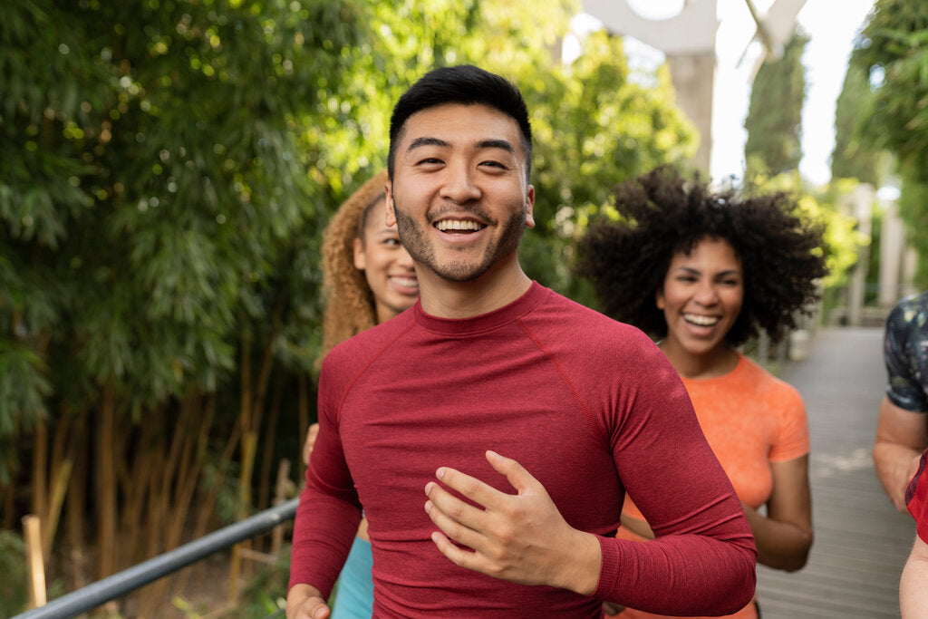 Group of friends running outdoors, with a man in front wearing a red UPF 50+ shirt, showing how activewear can provide sun protection.