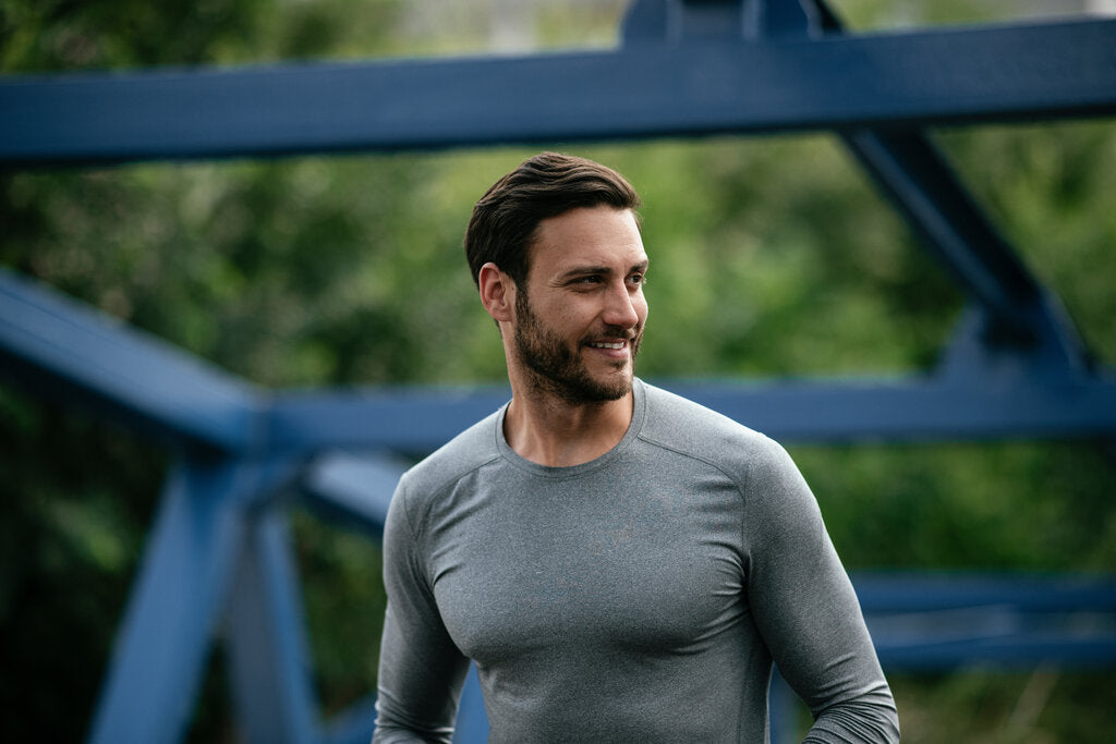 Smiling man wearing a fitted gray UPF long-sleeve shirt outdoors, highlighting sun-protective activewear for outdoor activities.