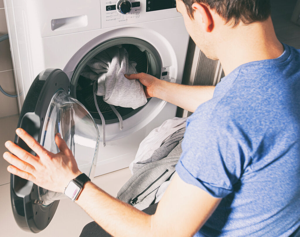 Person loading clothing into a washing machine, illustrating how washing and care habits can affect the durability of UV protection in UPF clothing over time.