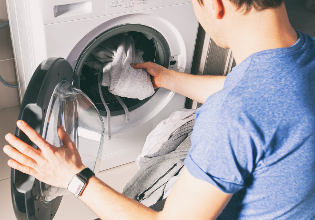 Man loading clothes into a washing machine, showing that high-quality UPF clothing is safe to wash and retains its sun protection when cared for properly.