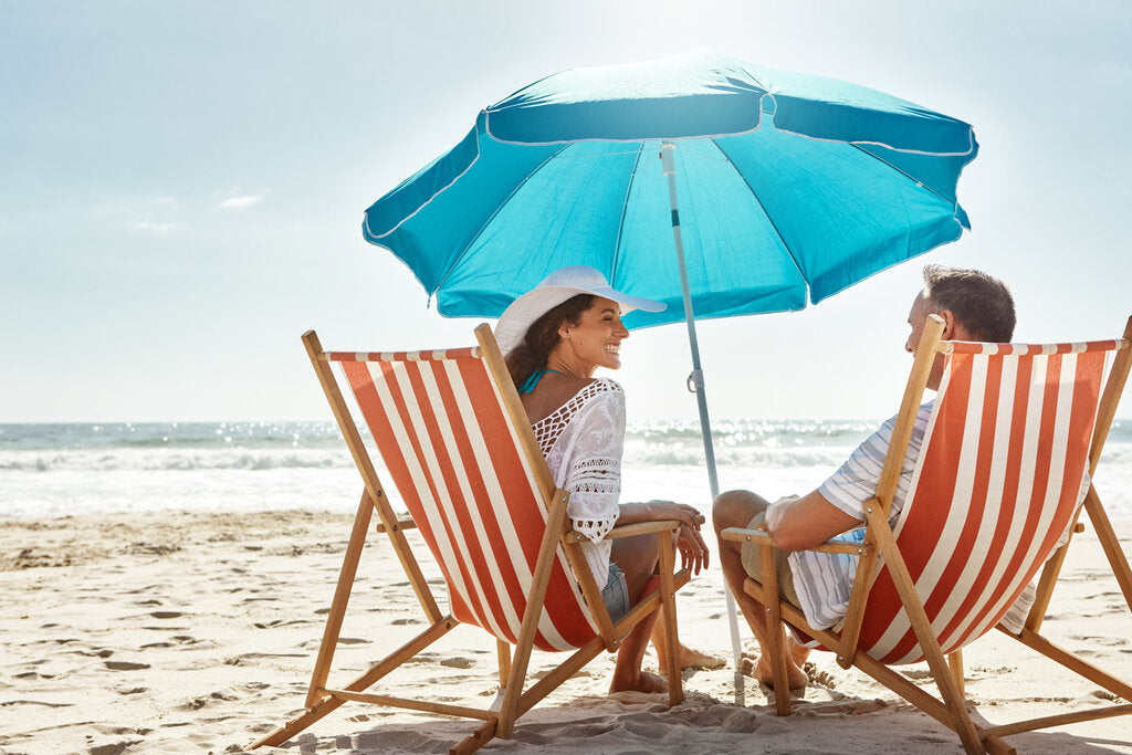 Couple relaxing on a sunny Florida beach under a large umbrella, highlighting the use of shade and sun-protective clothing as key strategies for UV protection in summer.