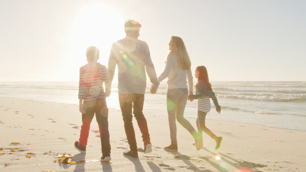 Family walking along a sunny Florida beach wearing UPF 50+ clothing, showing how consistent UV protection helps prevent cumulative sun damage and supports lifelong skin health.