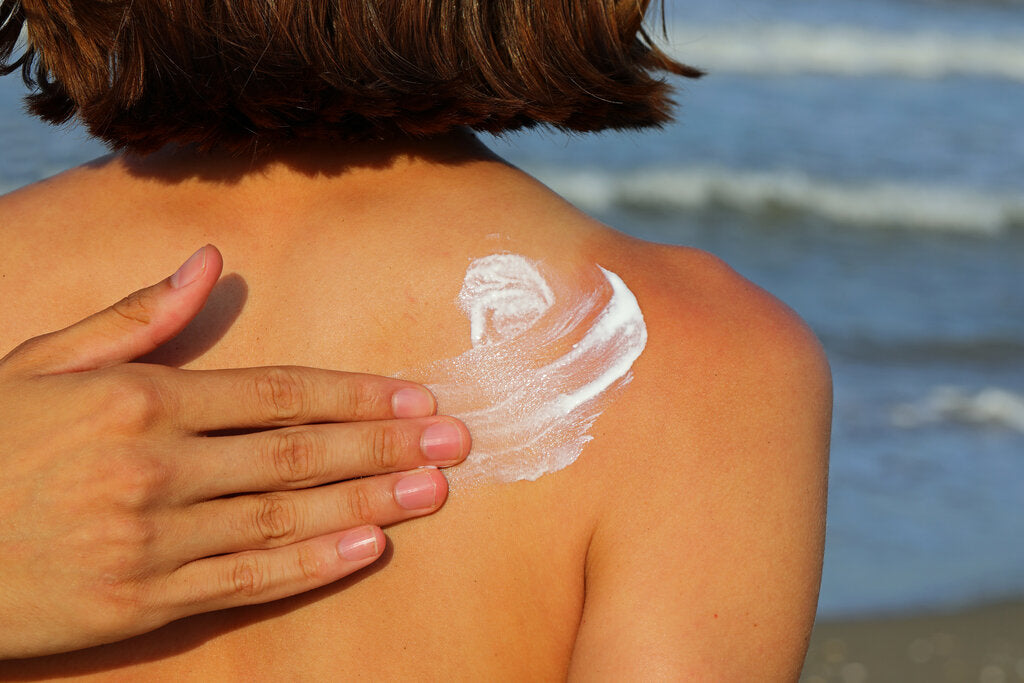 Applying sunscreen to a shoulder at the beach, highlighting the need for reapplication to maintain sun protection.