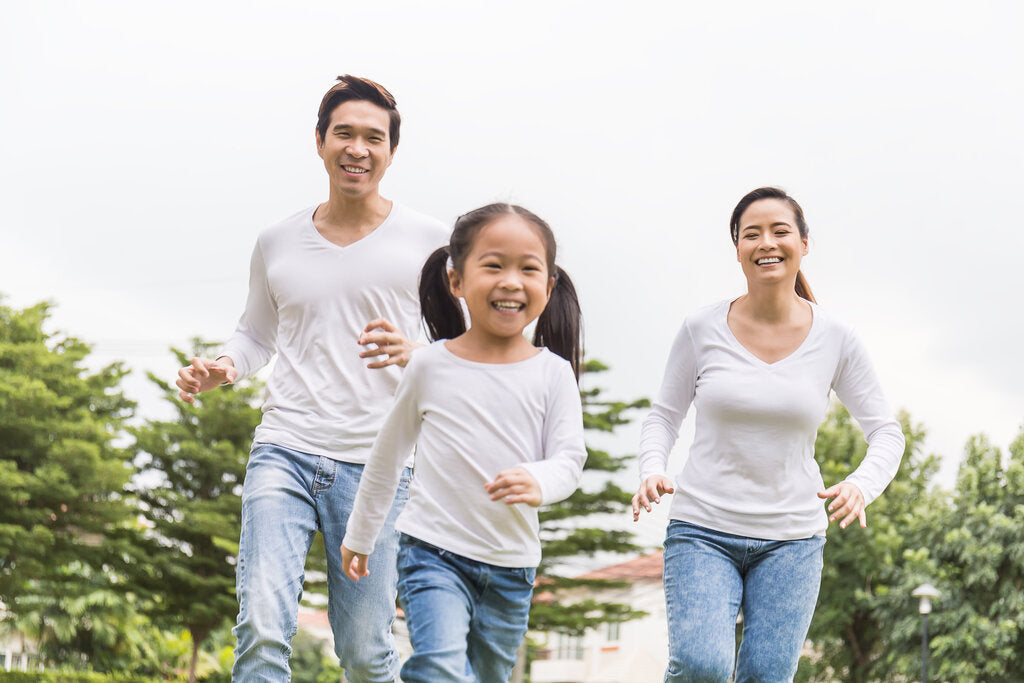 Happy family running outdoors in matching white long-sleeve UPF shirts and jeans, showcasing sun-protective clothing for active lifestyles.