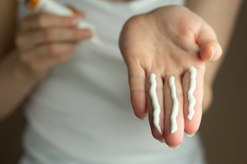 Close-up of a person dispensing three finger-length strips of sunscreen onto their hand, emphasizing the recommended amount for proper sun protection.