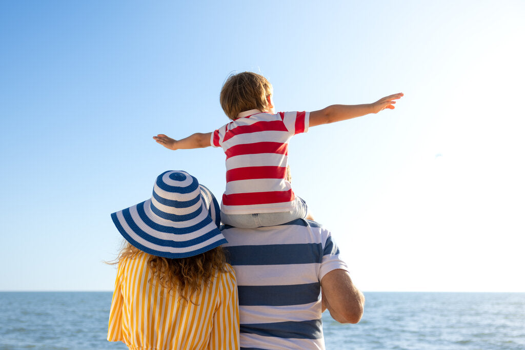 Family enjoying a sunny day at the beach, showing the need for sun-safe habits like UPF clothing, wide-brim hats, and sunscreen to protect against UV rays.