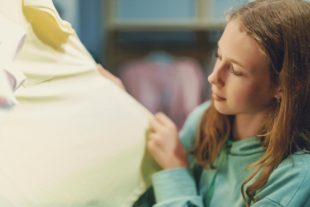 Young girl examining a pastel yellow UPF shirt in a clothing store, checking the fabric quality and sun protection label.