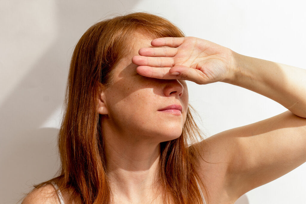 Woman shielding her eyes from bright sunlight with her hand, symbolizing the need for daily sun protection and awareness of cumulative UV damage over time.