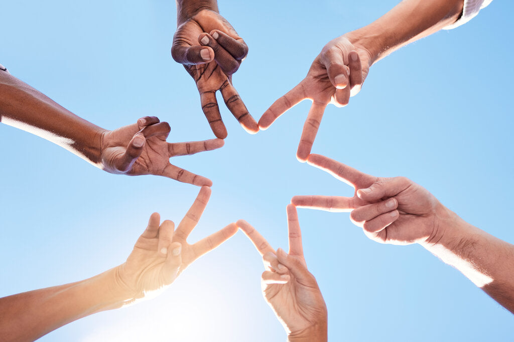 Group of diverse hands forming a star shape against a bright blue sky, symbolizing melanin diversity and the importance of sun protection for all skin tones.