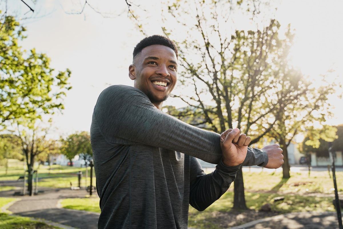 Smiling man stretching outdoors in a long-sleeve shirt, staying active under the sun.