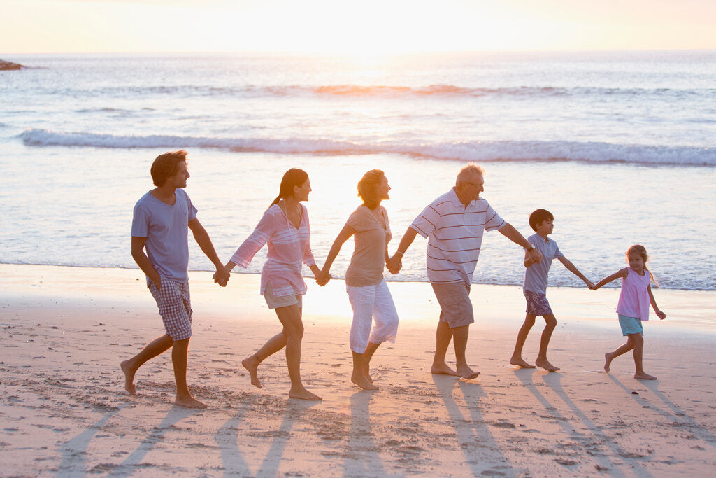 Multi-generational family walking along the beach at sunset, highlighting the importance of sun protection for all ages, from kids to parents and grandparents.