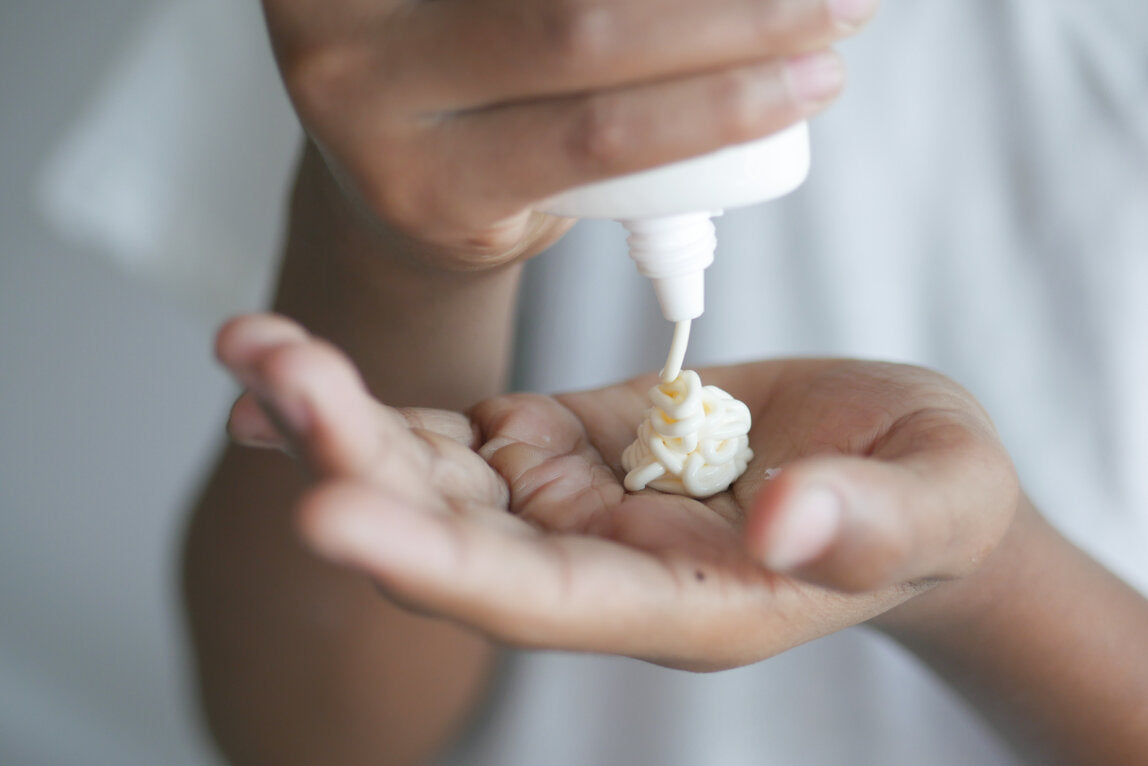 Close-up of a person squeezing a generous amount of sunscreen into their palm from a white bottle.