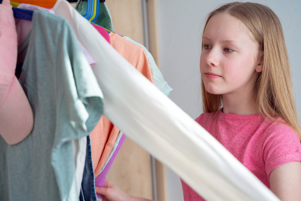 Young girl choosing clothes from her closet, illustrating the importance of selecting UPF clothing for daily sun protection.