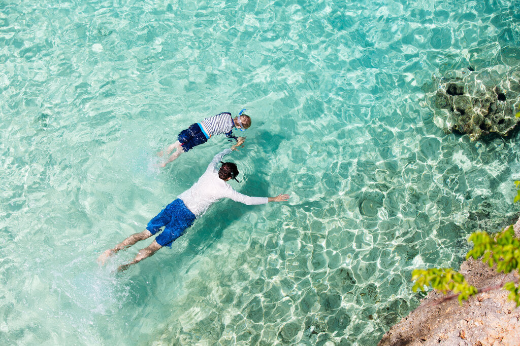 Parent and child snorkeling in rash guards, covering up as a reef-safe alternative to sunscreen in the water.