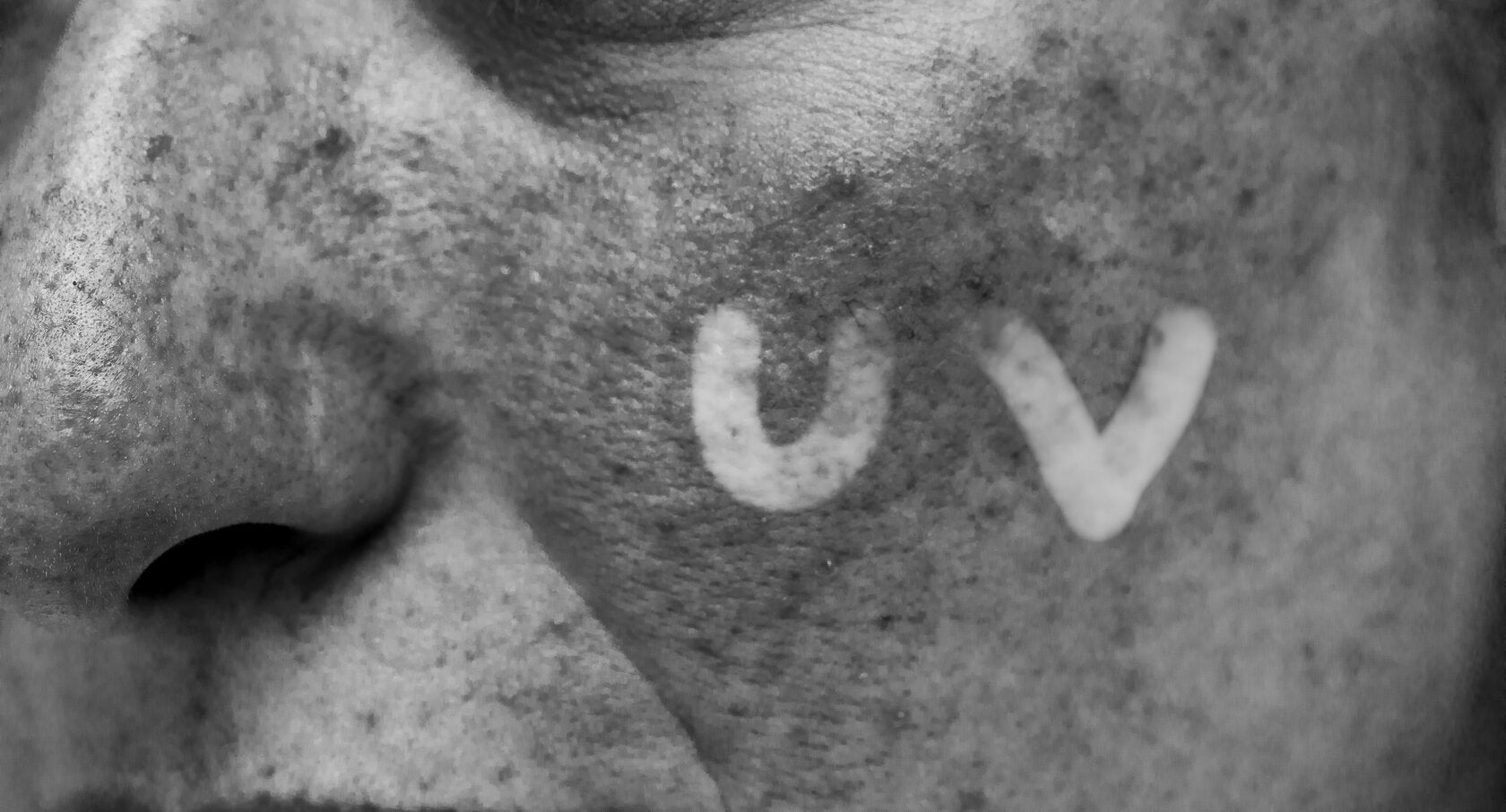 Close-up of a person’s face under UV light, revealing sun damage and the letters 'UV' written on their skin to highlight the effects of ultraviolet exposure.