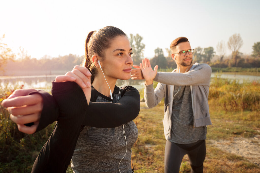Two active individuals stretching outdoors in UPF clothing, preparing for exercise while staying protected from UV exposure.