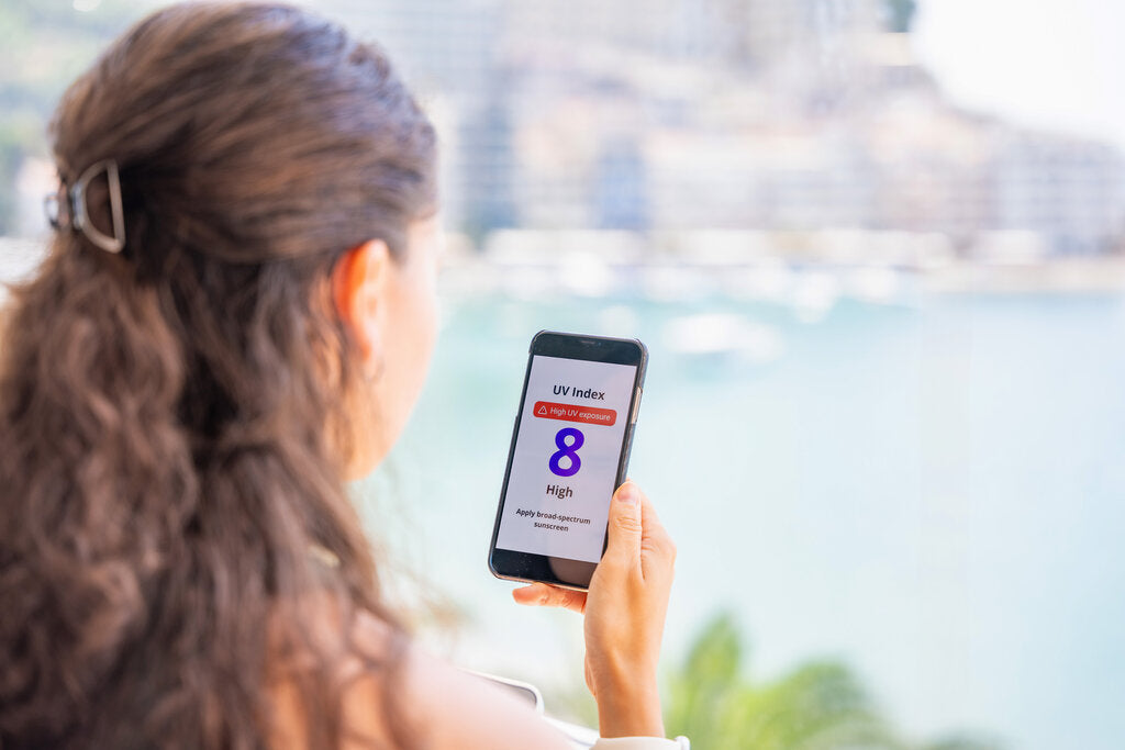 Person checking the UV Index on a smartphone near the water, highlighting the importance of monitoring UV levels as a daily skin protection habit.
