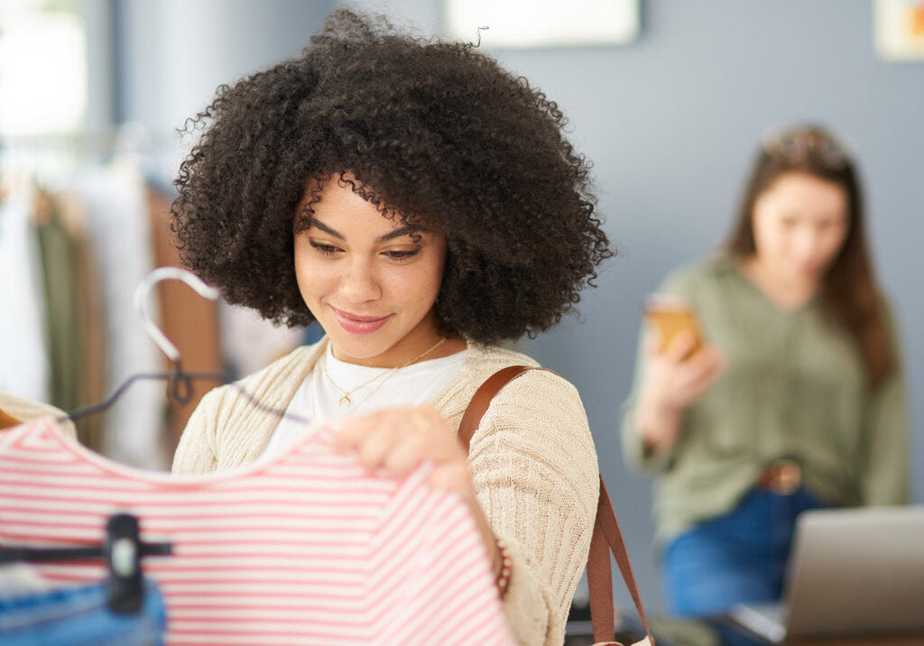 Young woman browsing UPF clothing in a store, examining a striped shirt while considering sun protection benefits.