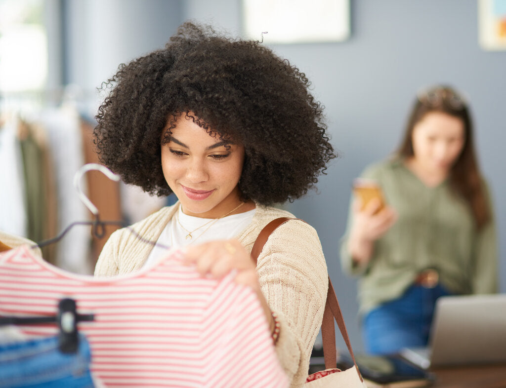 Young woman browsing UPF clothing in a store, examining a striped shirt while considering sun protection benefits.