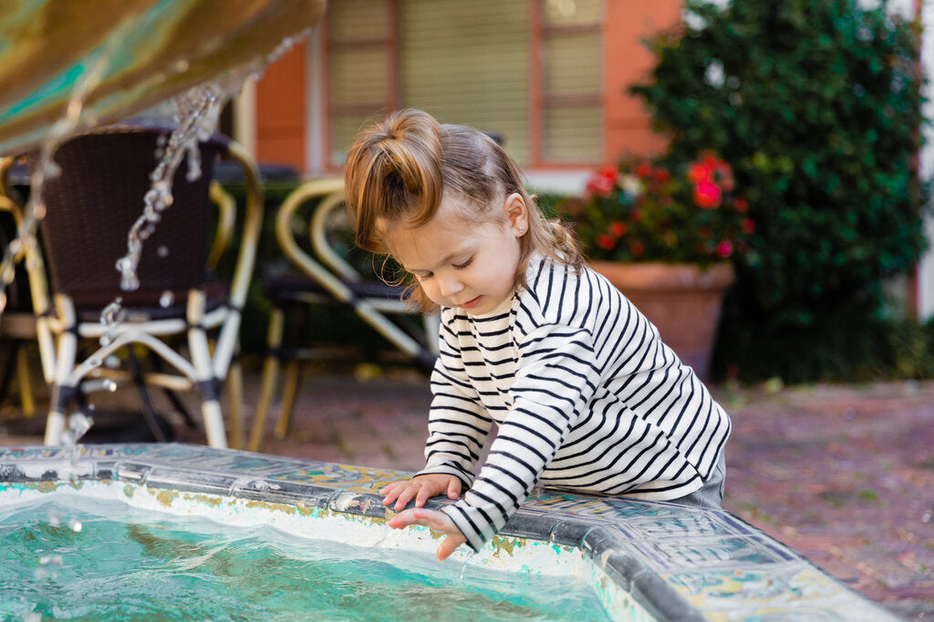 Young child wearing sun-protective clothing while playing at an outdoor fountain.